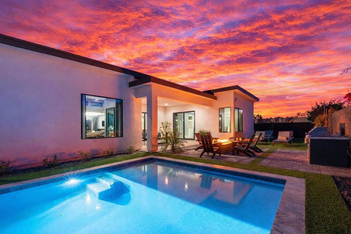 Modern single-story house at dusk with illuminated pool and outdoor seating around a fire pit. PT-105