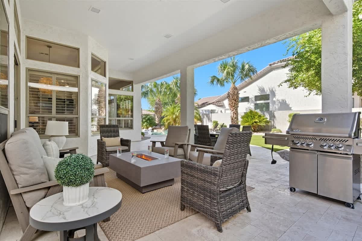 The serene backyard boasts a pool, hot tub, fire pit with surrounding seating, a BBQ grill, an outdoor dining table for four, and an open grassy area for relaxation and play.