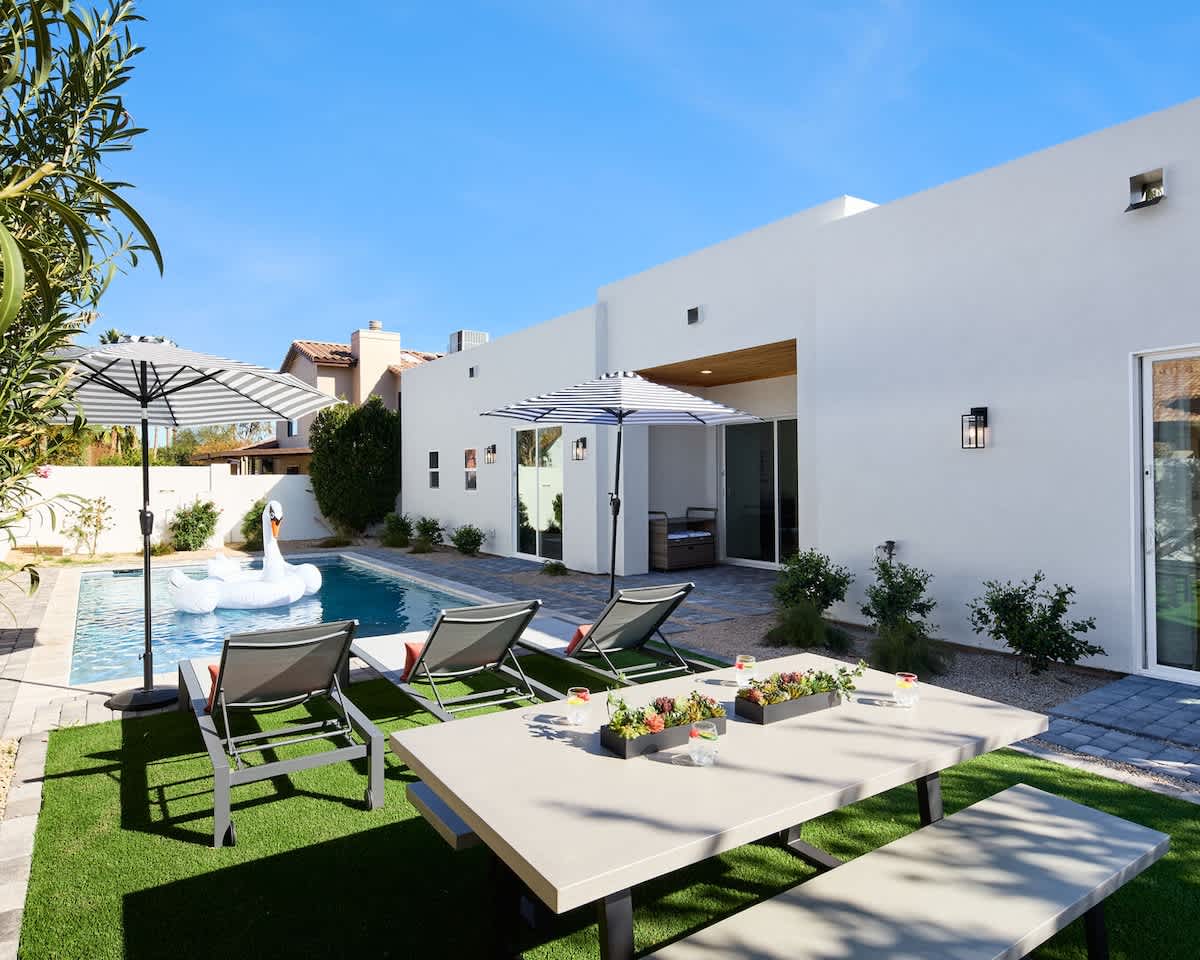 Beautiful backyard featuring a sparkling blue heated pool, sun loungers with umbrellas, and an outdoor dining table to accommodate 6 guests.