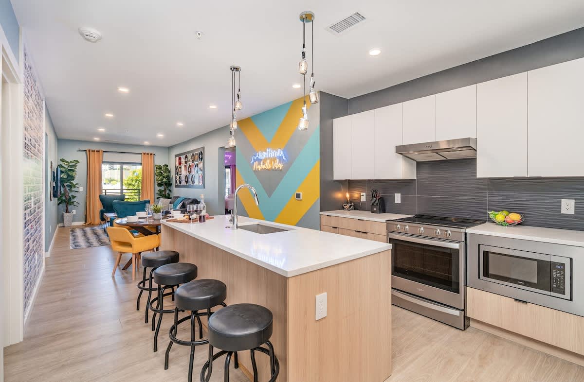 Full kitchen with stainless steel appliances, pristine white countertops, light wood and white cabinetry, and a spacious island with breakfast bar seating for four.