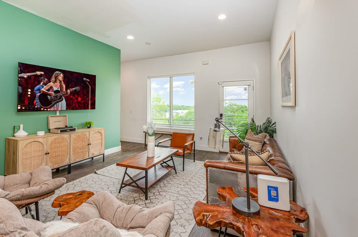 Welcoming living area with a vibrant green accent wall, large Smart TV, and plush seating arranged to take in the serene outside views.