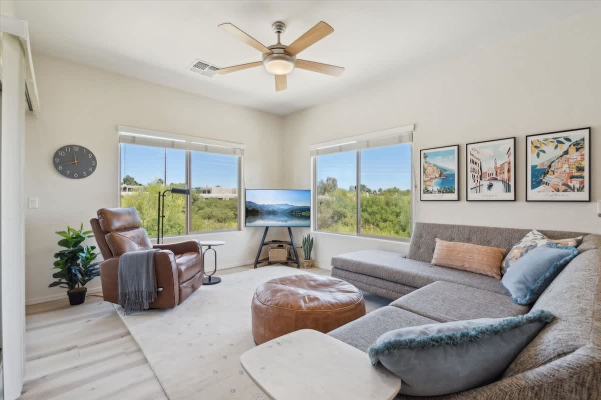 The Living Room is a bright space with plush seating, a Smart TV, and peaceful green views through large windows.
