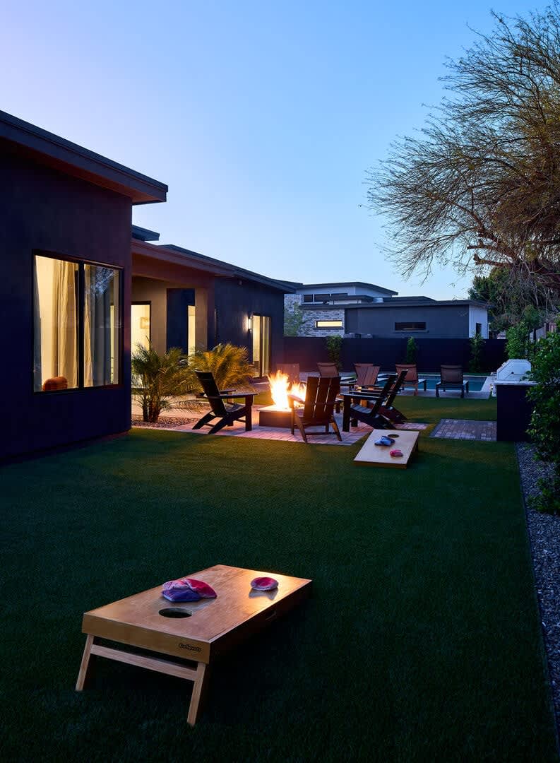 Resort-like backyard with a covered patio offering outdoor dining, a sparkling blue heated pool with sun loungers, yard games, a BBQ grill and a fire pit.