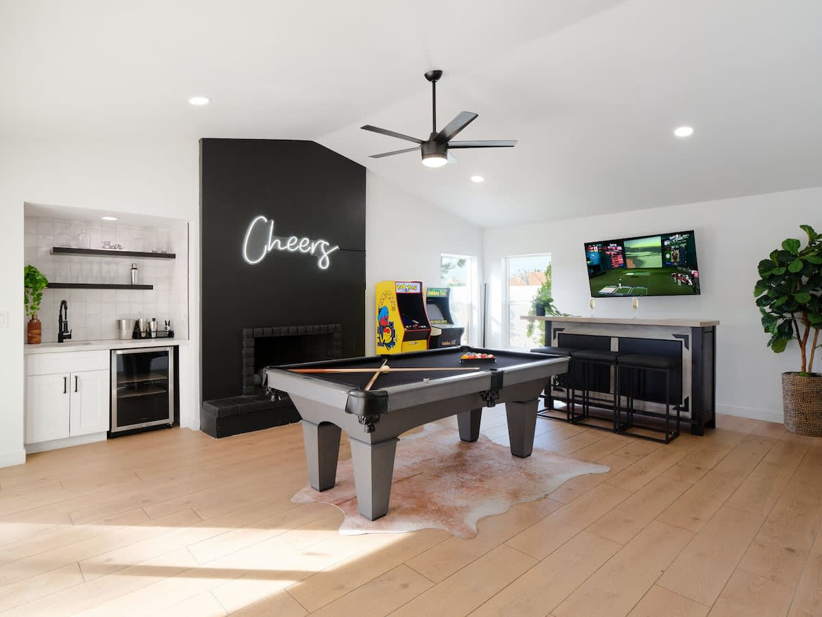 Game room featuring a pool table, wet bar with a mini fridge, arcade games, a smart TV with bar seating, and backyard access.