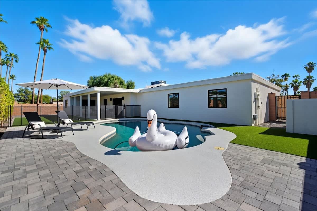 Backyard oasis featuring a sparkling pool, sun loungers, and a covered patio with a comfortable lounge area and outdoor dining table for six.