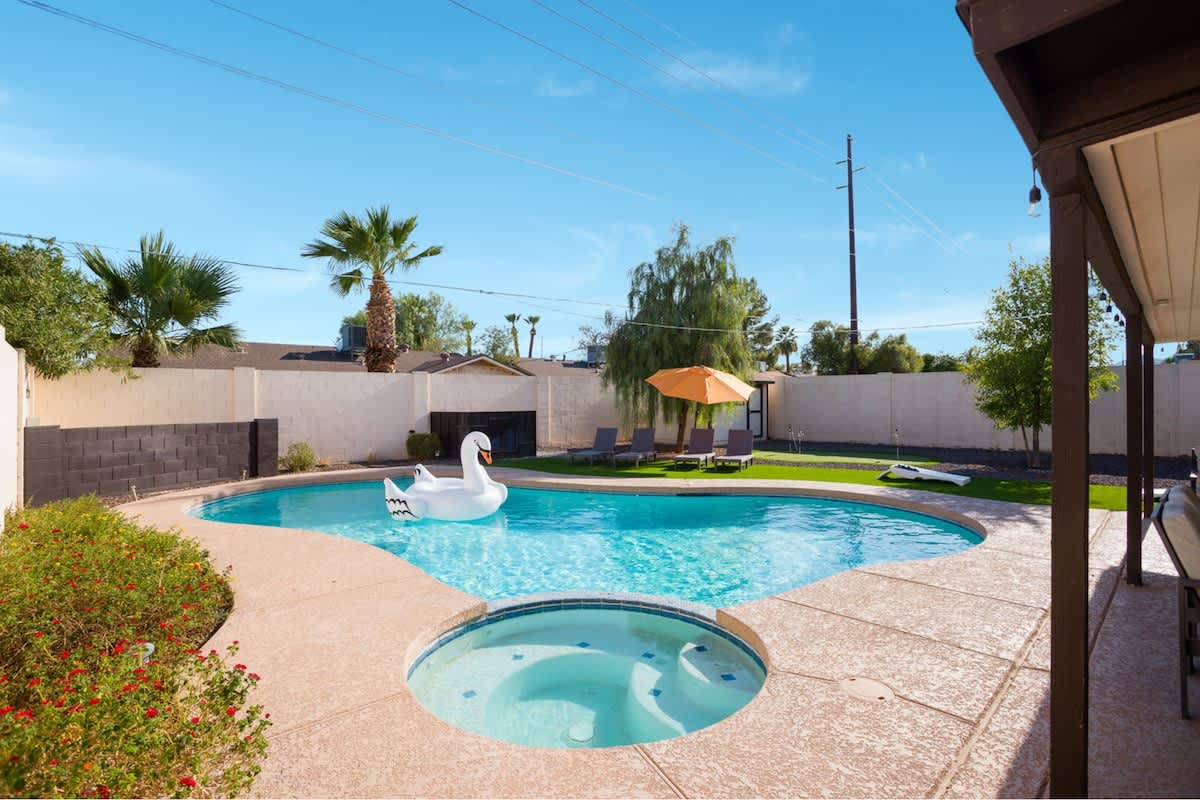 Resort-style backyard with a sparkling pool, hot tub, sun loungers, private patio with outdoor dining and seating, grill, mini golf, and corn hole.