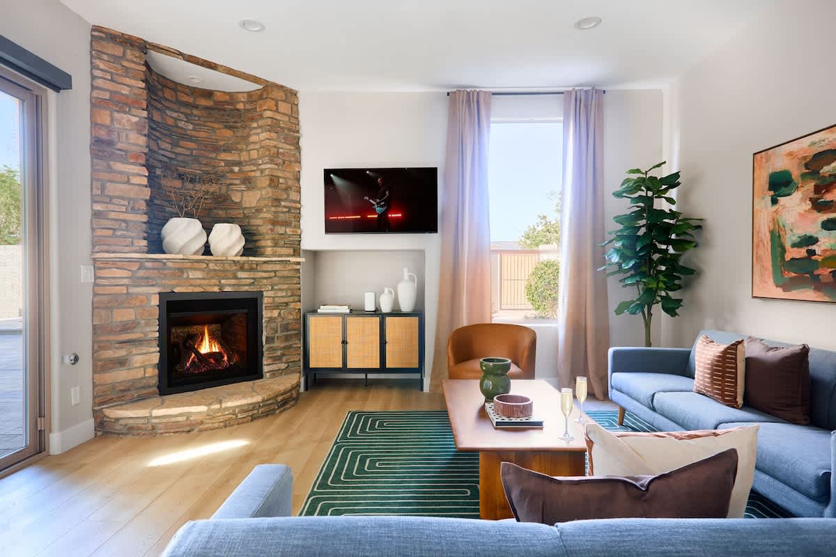 Living room with cozy seating, modern décor, and a gas fireplace, brightened by natural light and views of the backyard.