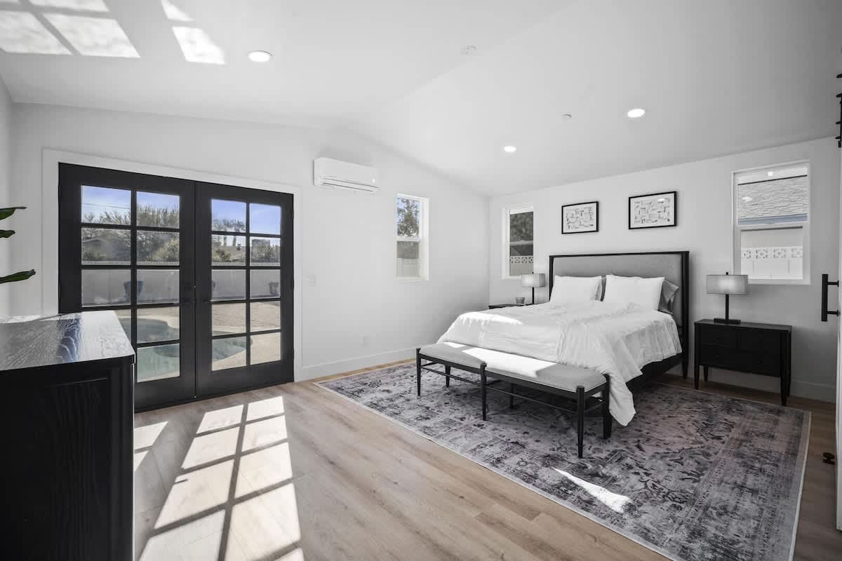 Bright and serene primary bedroom featuring a plush king bed, modern furnishings, French doors to the backyard, and a private en-suite bathroom.