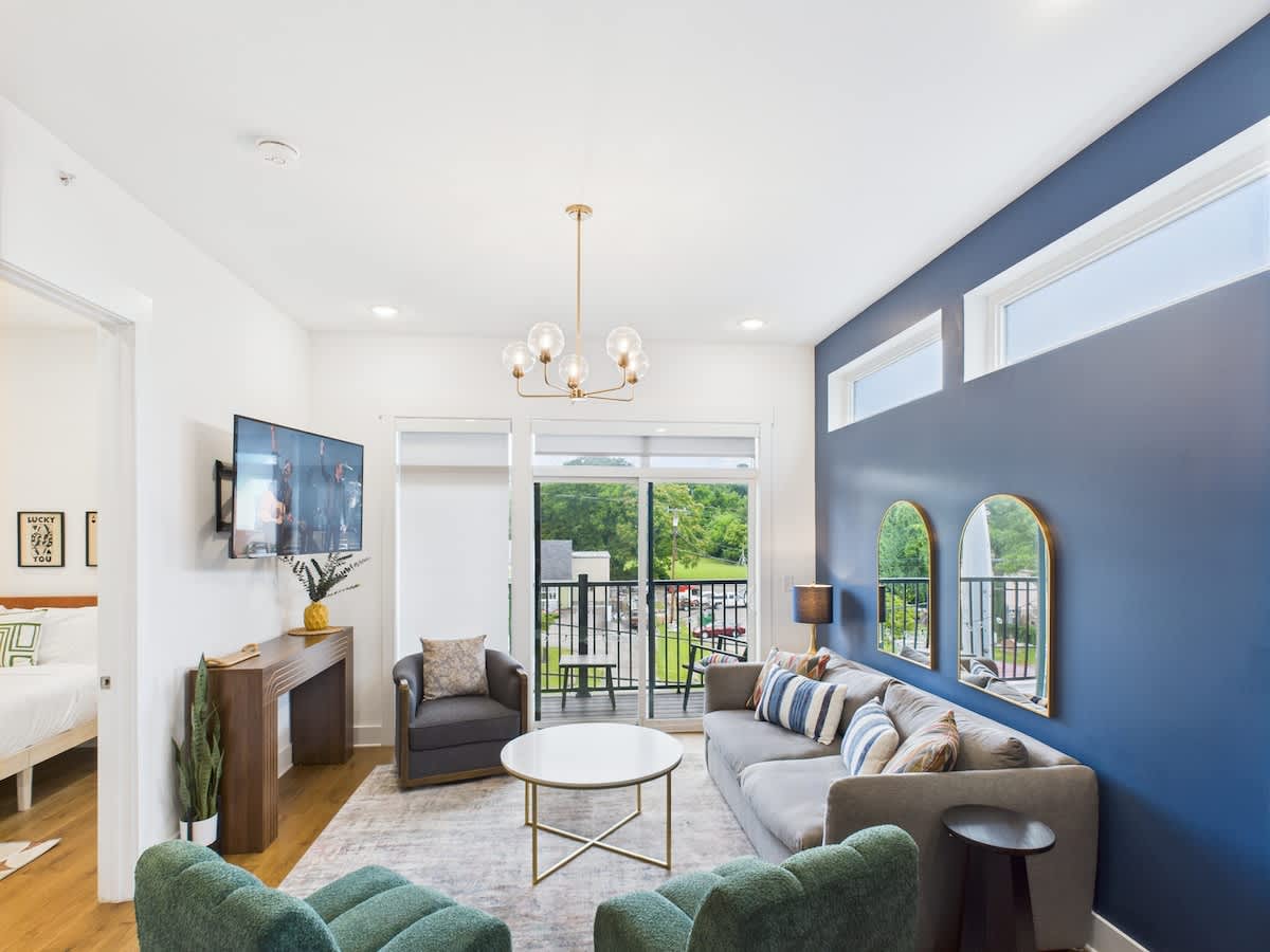 Bright open floor living space featuring a smart flat-screen TV, designer furnishings, and a private balcony entrance.