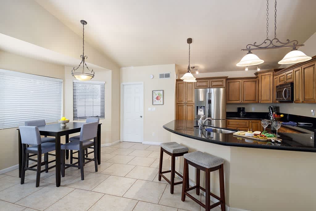 Fully equipped kitchen with stainless steel appliances, breakfast bar seating, and dining table with seating for 4 guests.