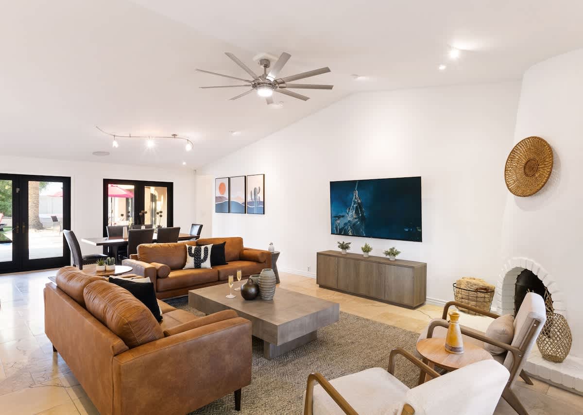 Bright open floor living space featuring a smart flat-screen TV, designer furnishings, and access to the outdoor patio leading to the attached casita and pool/spa area. Fireplace not functional.