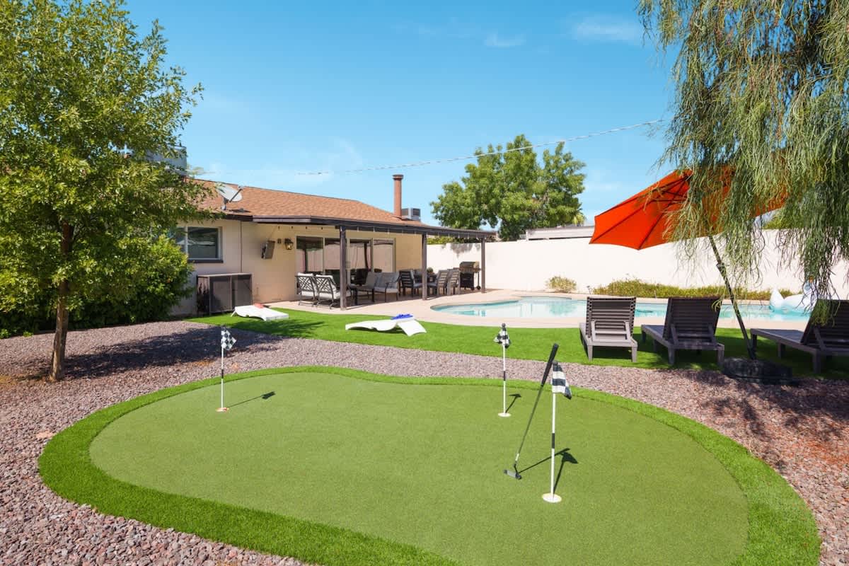 Resort-style backyard with a sparkling pool, hot tub, sun loungers, private patio with outdoor dining and seating, grill, mini golf, and corn hole.