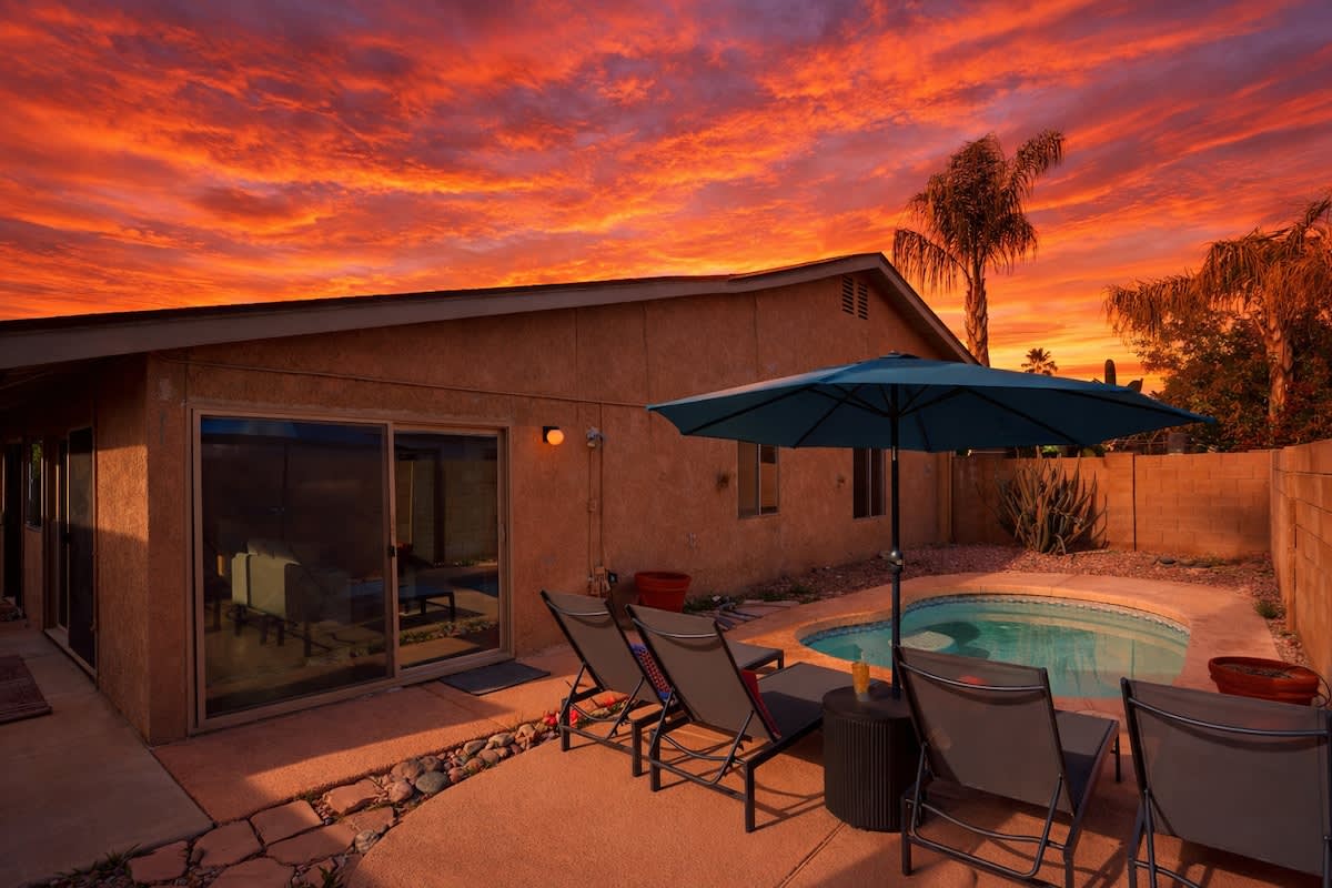 Private backyard with a sparkling pool, sun loungers, outdoor dining area with seating for 8 guests and a lounge area surrounding a fire pit.