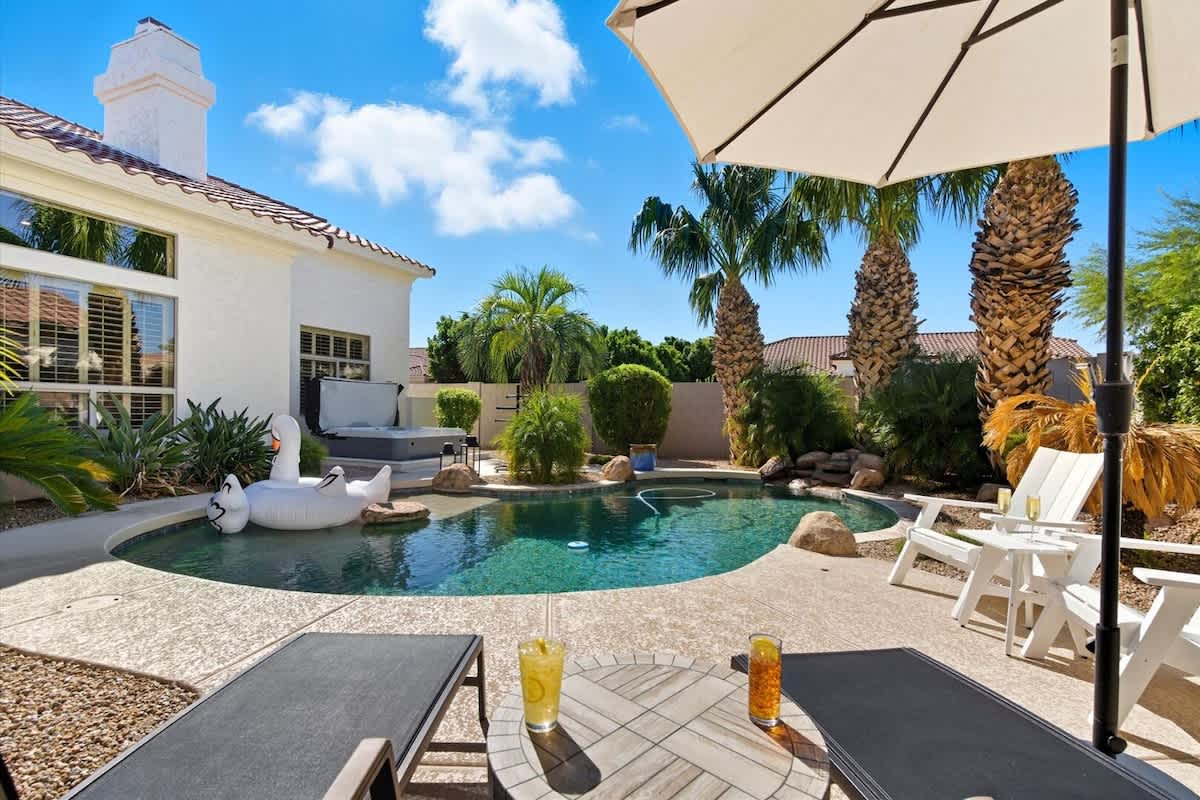 The serene backyard boasts a pool, hot tub, fire pit with surrounding seating, a BBQ grill, an outdoor dining table for four, and an open grassy area for relaxation and play.