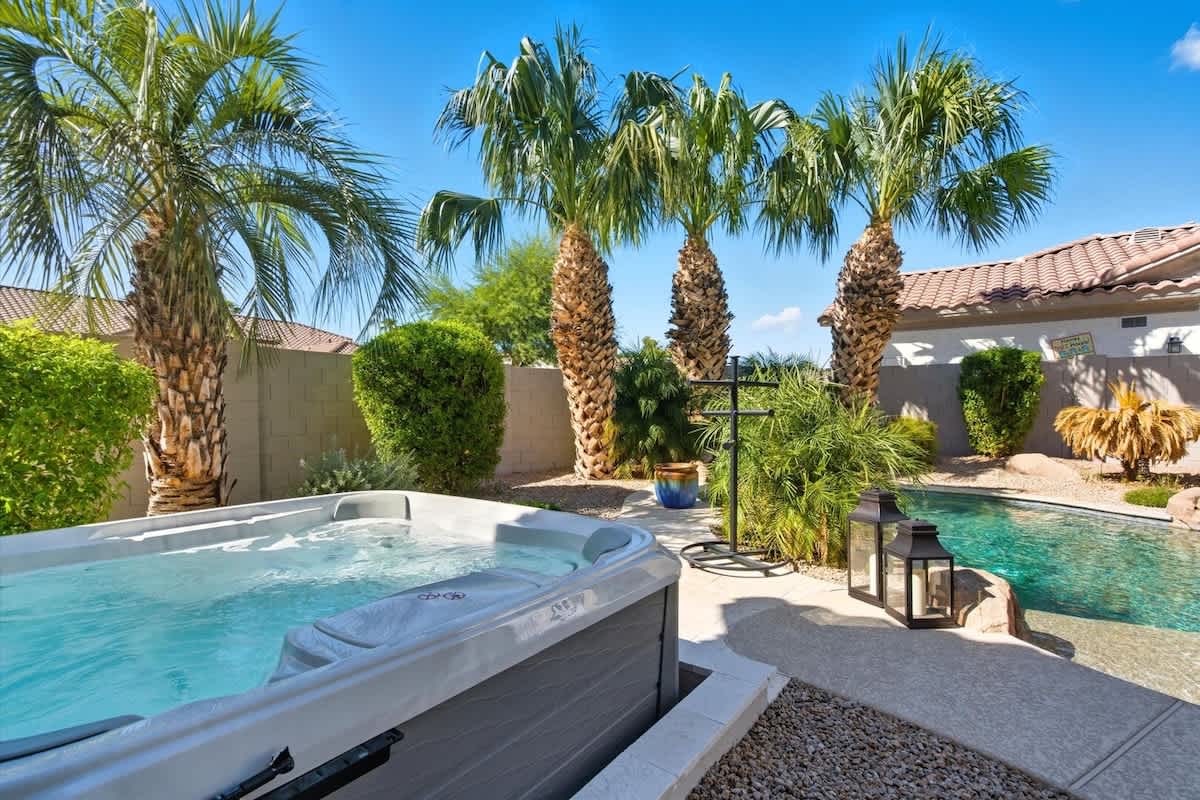 The serene backyard boasts a pool, hot tub, fire pit with surrounding seating, a BBQ grill, an outdoor dining table for four, and an open grassy area for relaxation and play.