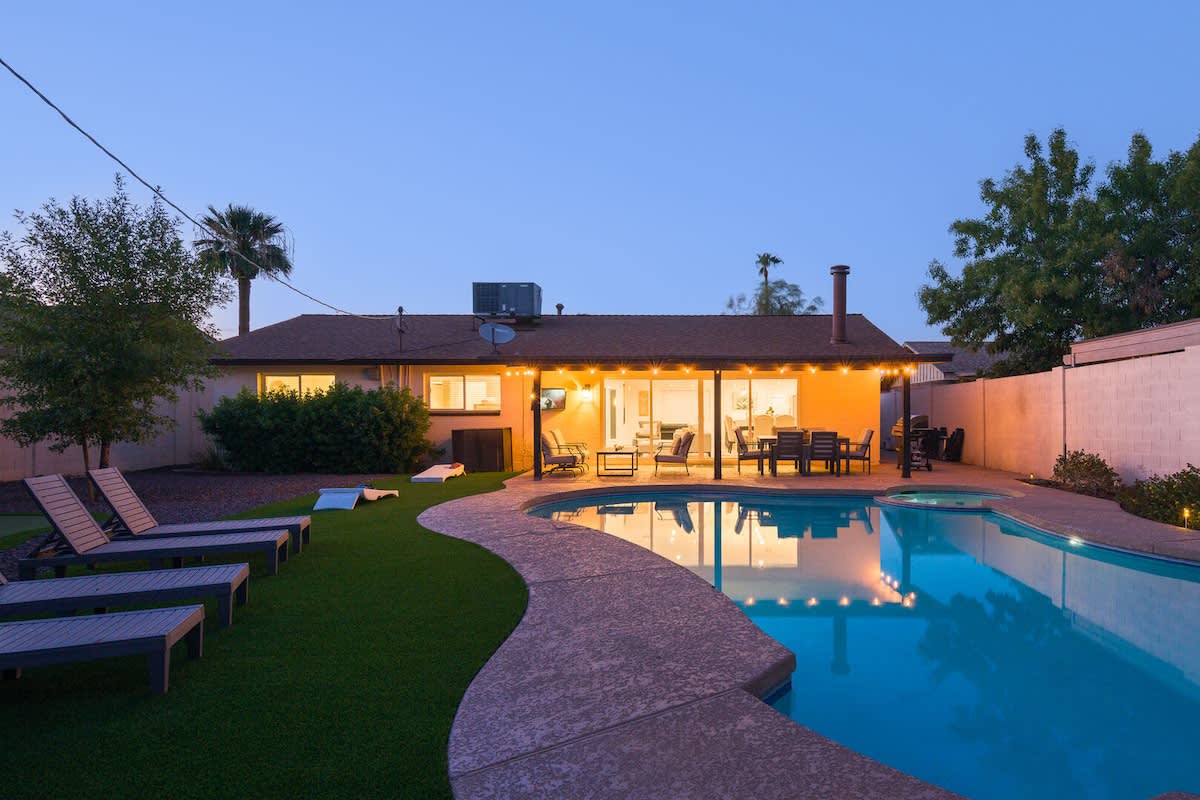 Resort-style backyard with a sparkling pool, hot tub, sun loungers, private patio with outdoor dining and seating, grill, mini golf, and corn hole.