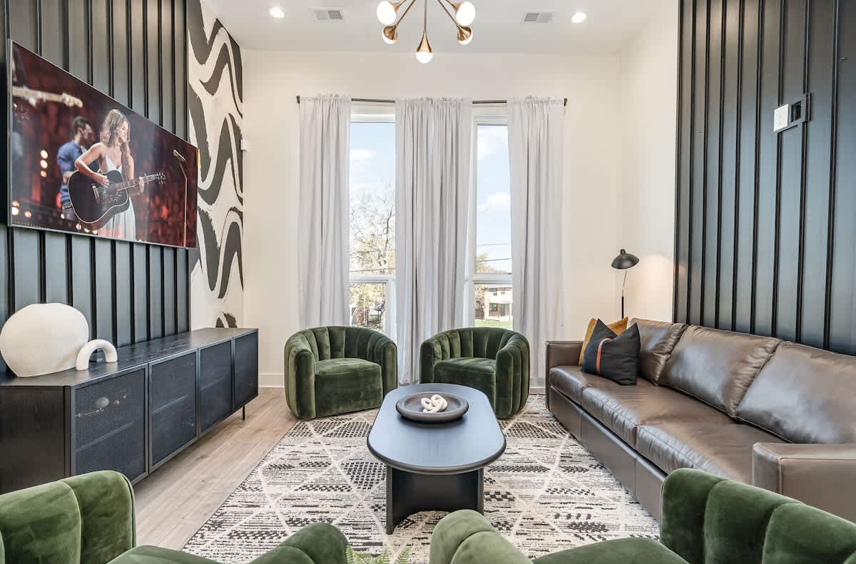 A modern, trendy living room adorned in designer furnishings and decor with sky-high ceilings, large windows, and a smart TV. (1st Floor)