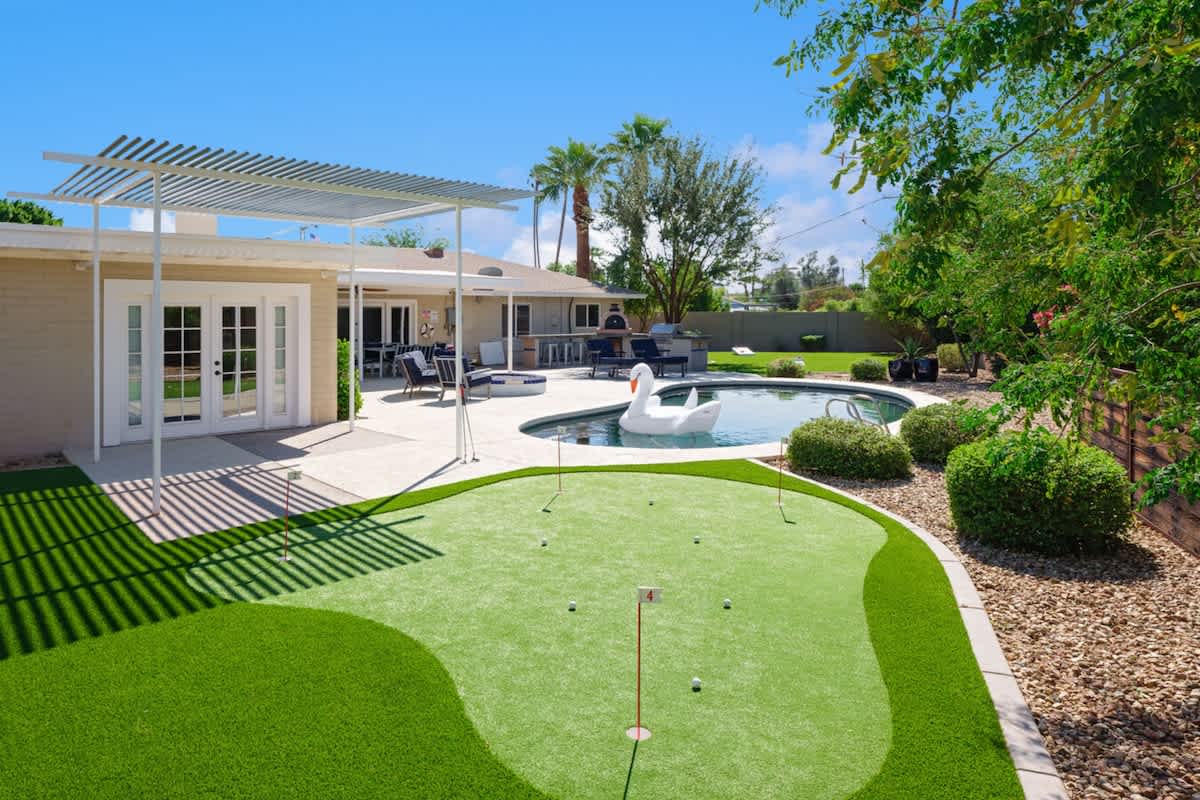 Large backyard featuring a covered patio with outdoor dining, fire pit with outdoor furnishings, heated pool, putting green, and a built-in BBQ and pizza oven.