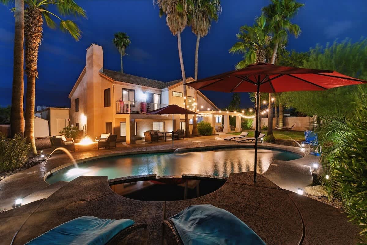 The private backyard is an entertainer’s dream with a pool, spa, fire pit, outdoor dining for six, built-in BBQ grill, hammock, pool loungers, cornhole, a large grassy area, and plenty of seating for 