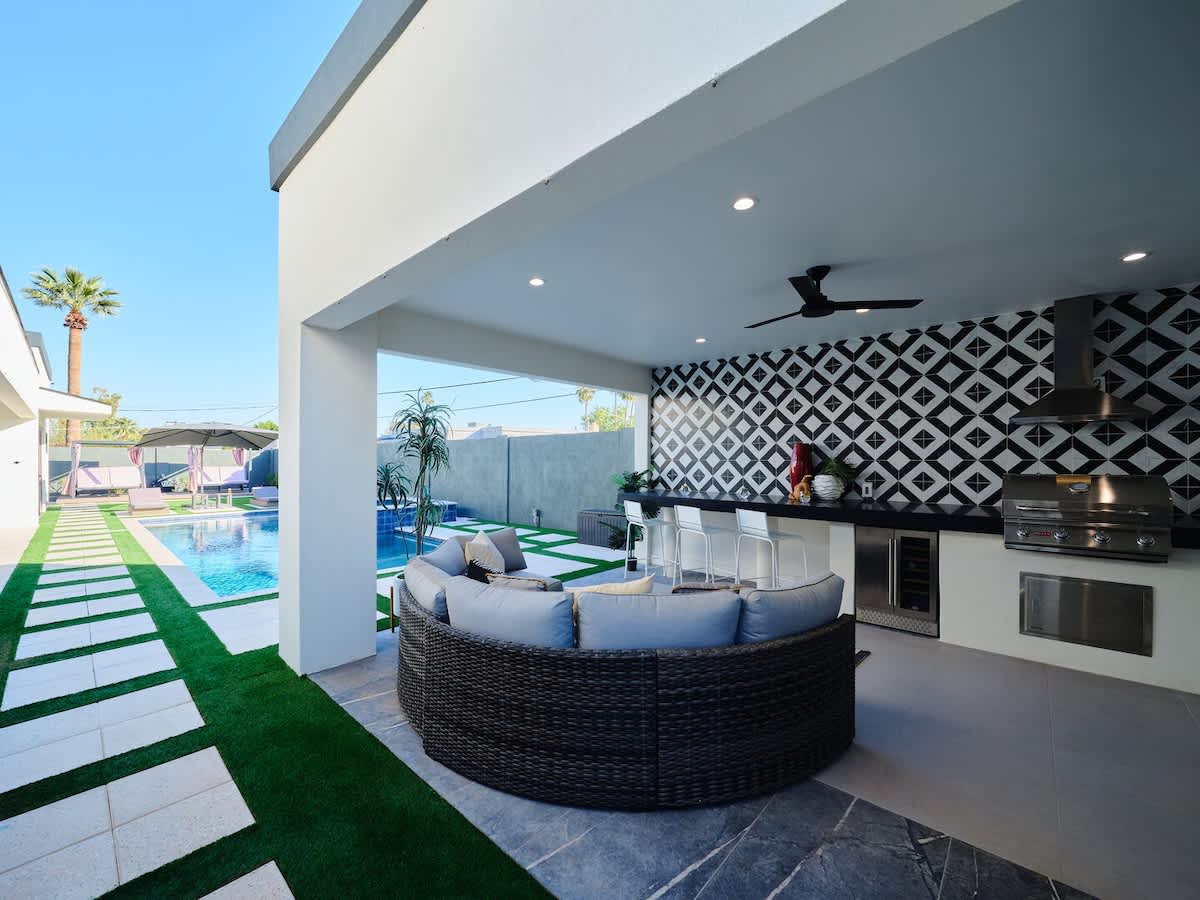 Resort-style backyard featuring a covered patio with outdoor dining, a sparkling blue heated pool and spa with sun loungers and cabanas, an outdoor kitchen with a built-in BBQ, mini fridge, and sink,