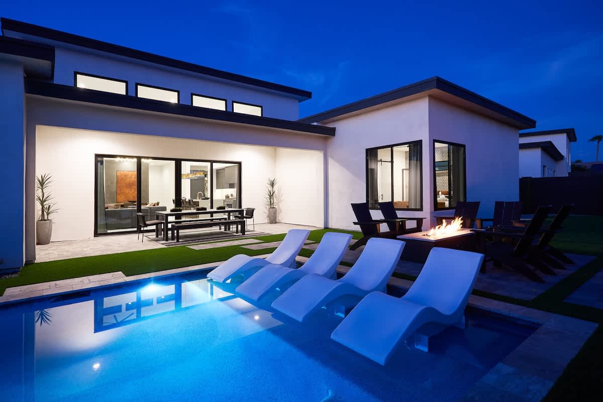 Resort-like backyard with a covered patio offering outdoor dining with seating for 8 guests, a sparkling blue heated pool with sun loungers, BBQ grill and a fire pit.