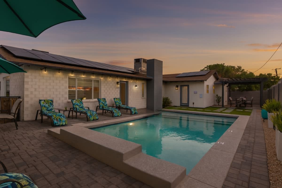 Stunning valley backyard featuring a sparkling blue heated pool with sun loungers, a BBQ grill, and outdoor dining while bistro lights set the mood.