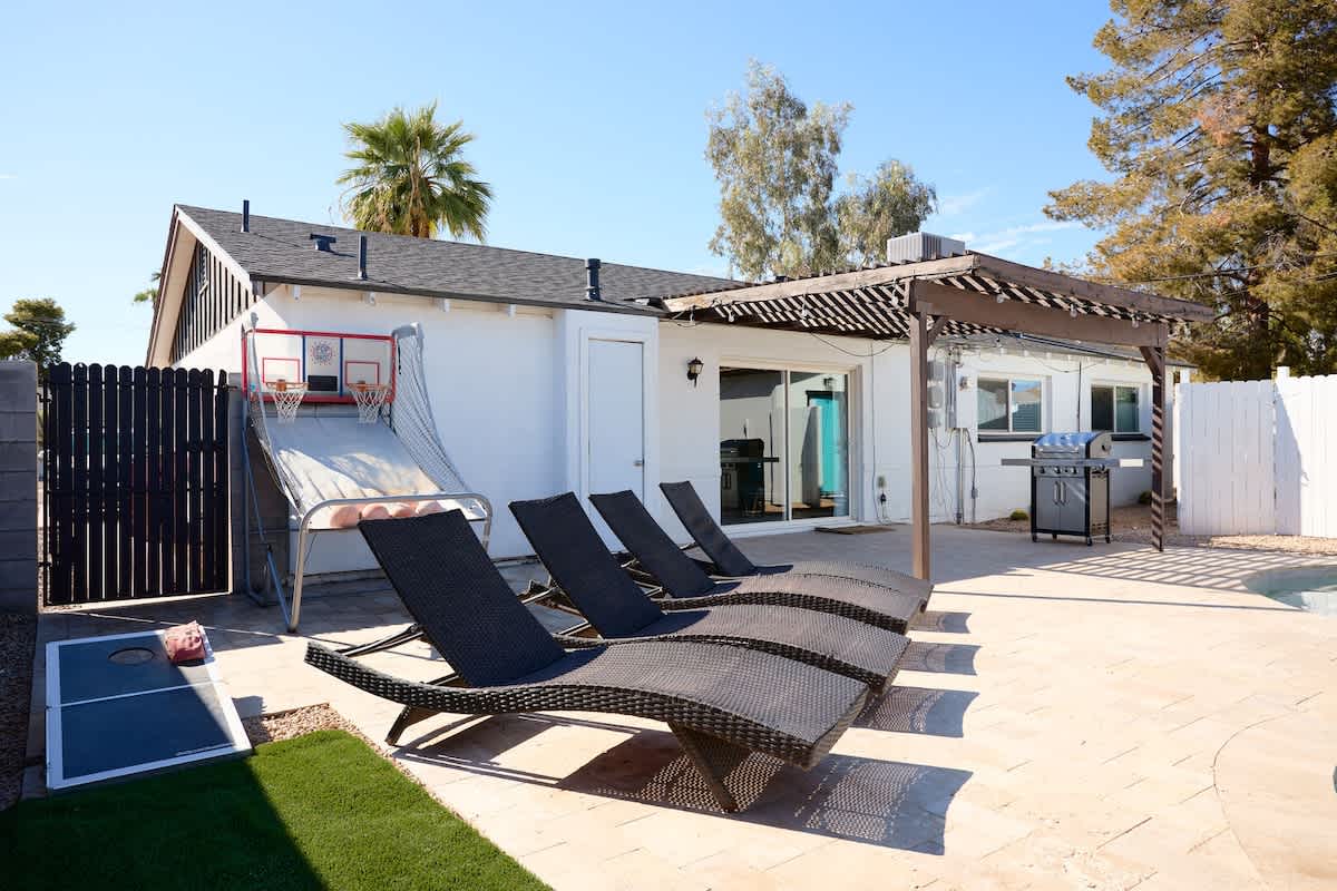 Backyard paradise with a sparkling pool, loungers, cornhole, and a basketball arcade game for non-stop fun.