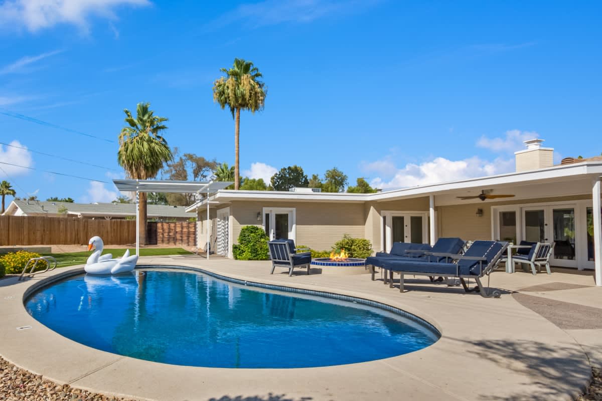 Large backyard featuring a covered patio with outdoor dining, fire pit with outdoor furnishings, heated pool, putting green, and a built-in BBQ and pizza oven.