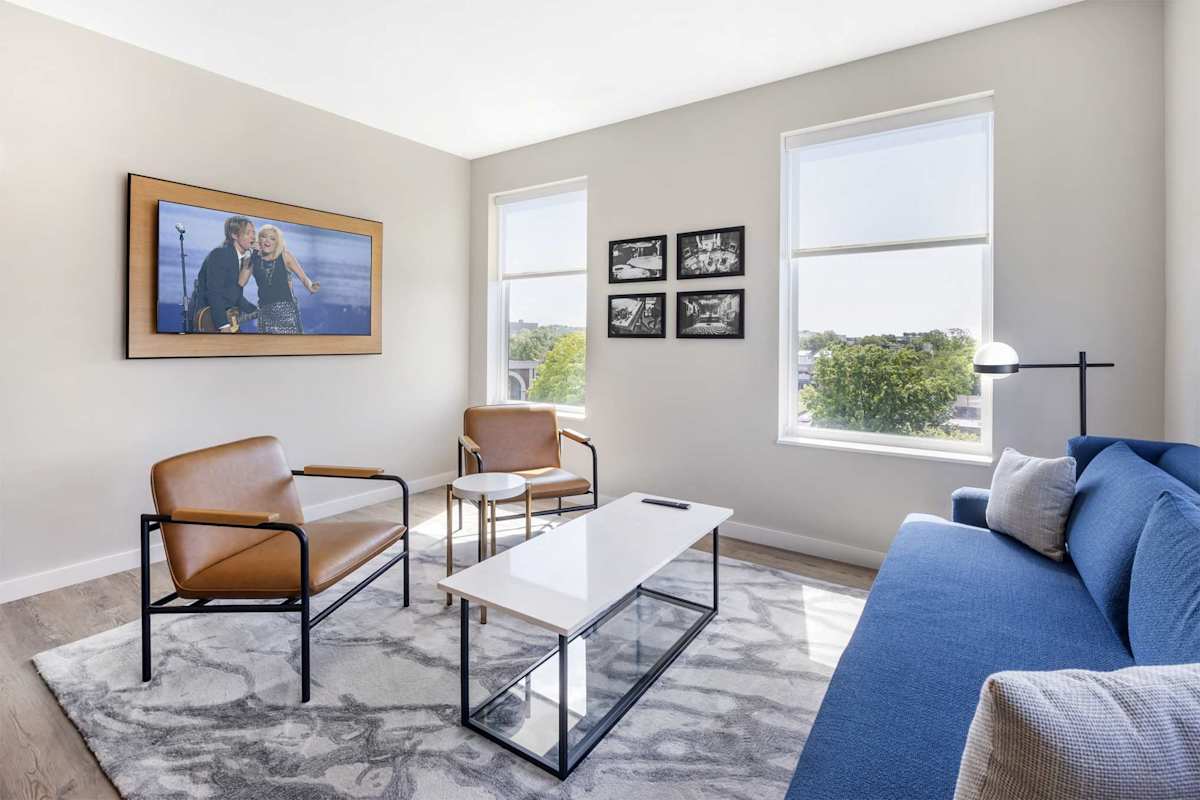 Bright, modern living room with a plush blue sofa, stylish leather seating, large windows, and a wall-mounted TV, perfect for relaxing after a day out.