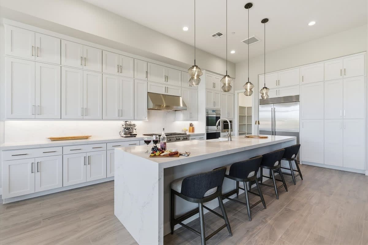 Full Kitchen features sleek white cabinetry, a spacious waterfall island with seating, and modern stainless steel appliances perfect for cooking and gathering.