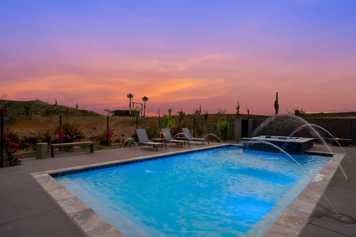 Stunning private oasis featuring a sparkling blue pool with sun loungers, a patio with a BBQ grill, outdoor furnishings for lounging and dining, and a fire pit surrounded by unparalleled desert views.