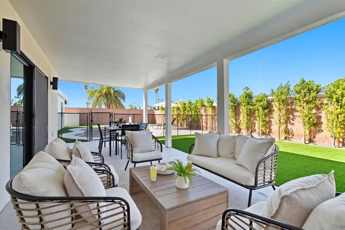 Backyard oasis featuring a sparkling pool, sun loungers, and a covered patio with a comfortable lounge area and outdoor dining table for six.