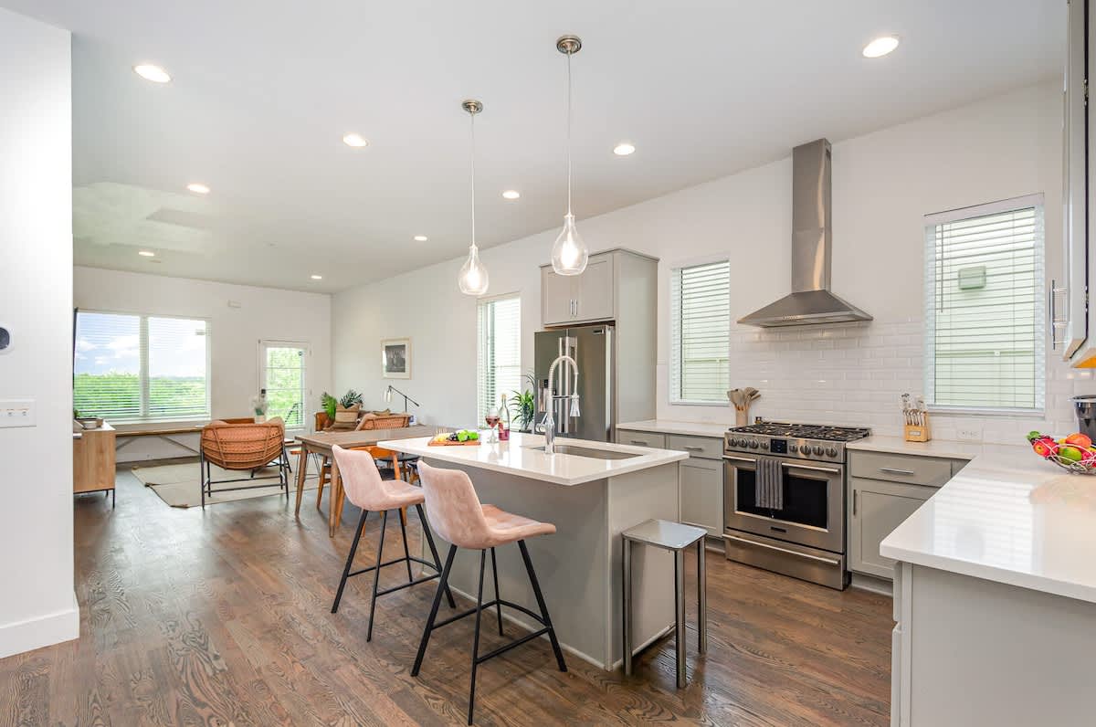 Bright open-concept kitchen featuring a quartz-topped island with bar seating, stainless steel appliances, and abundant natural light streaming through the windows.