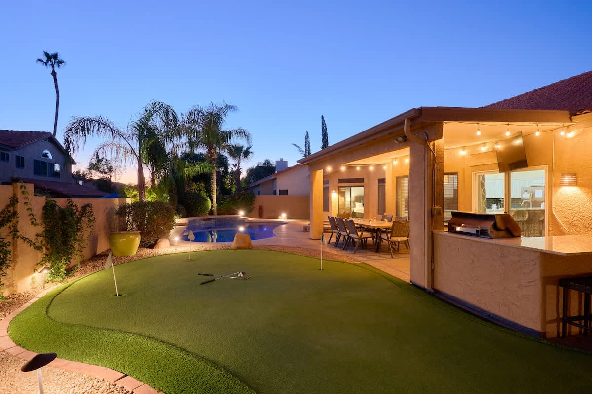 Private backyard paradise featuring a pool, sun loungers, mini golf, a covered patio with an outdoor dining area, and a BBQ with bar seating.