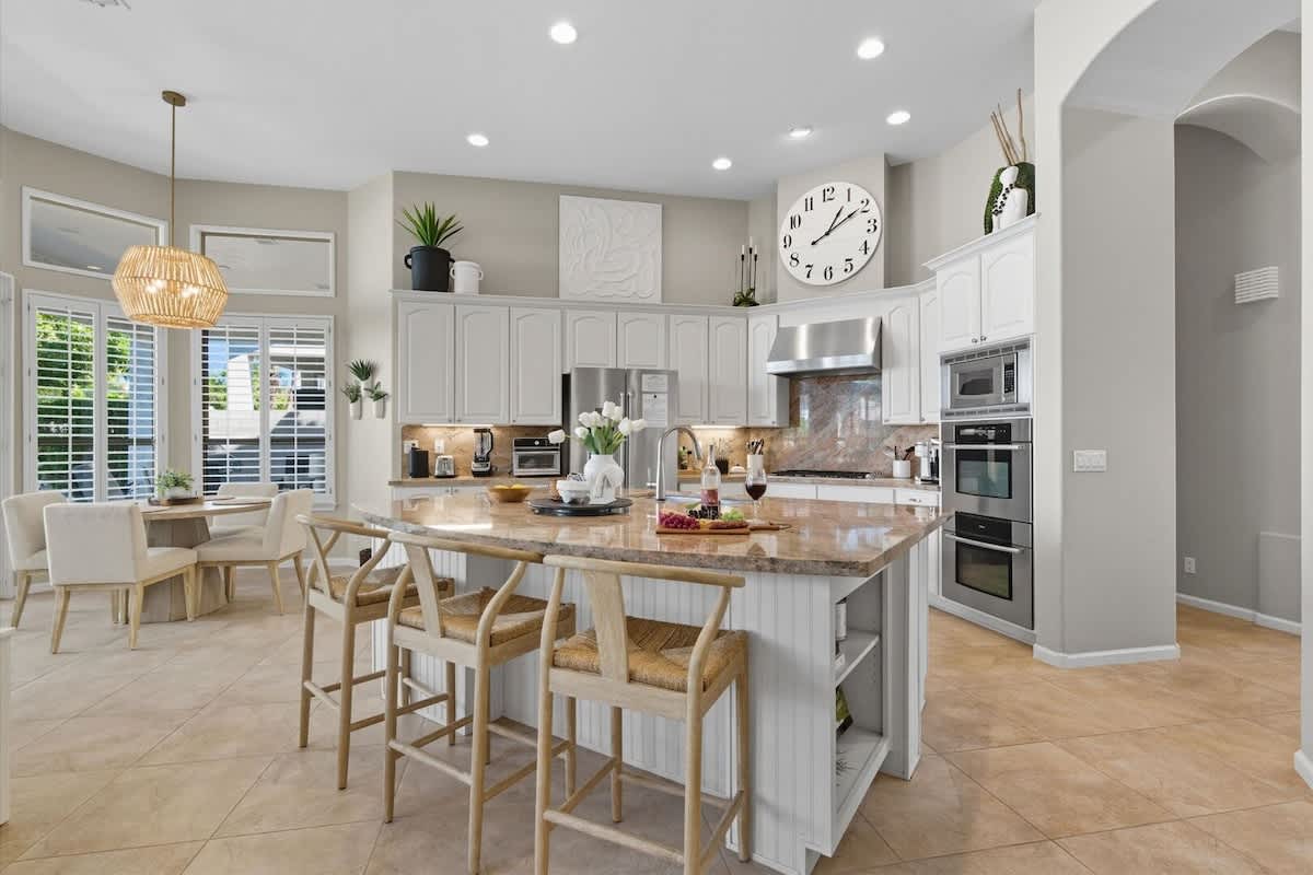 The kitchen showcases granite countertops, crisp white cabinets, stainless steel appliances, and a spacious island with breakfast bar seating for three.