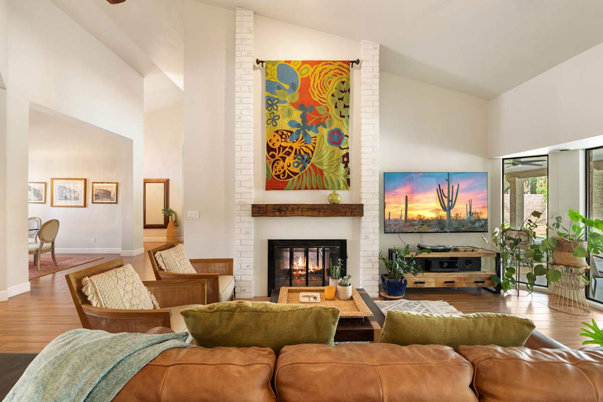 Unwind in this dual living room featuring two stylish lounging areas anchored by a double-sided white-brick fireplace, complete with a Smart TV, vaulted ceilings, and sunlit views toward the poolside 