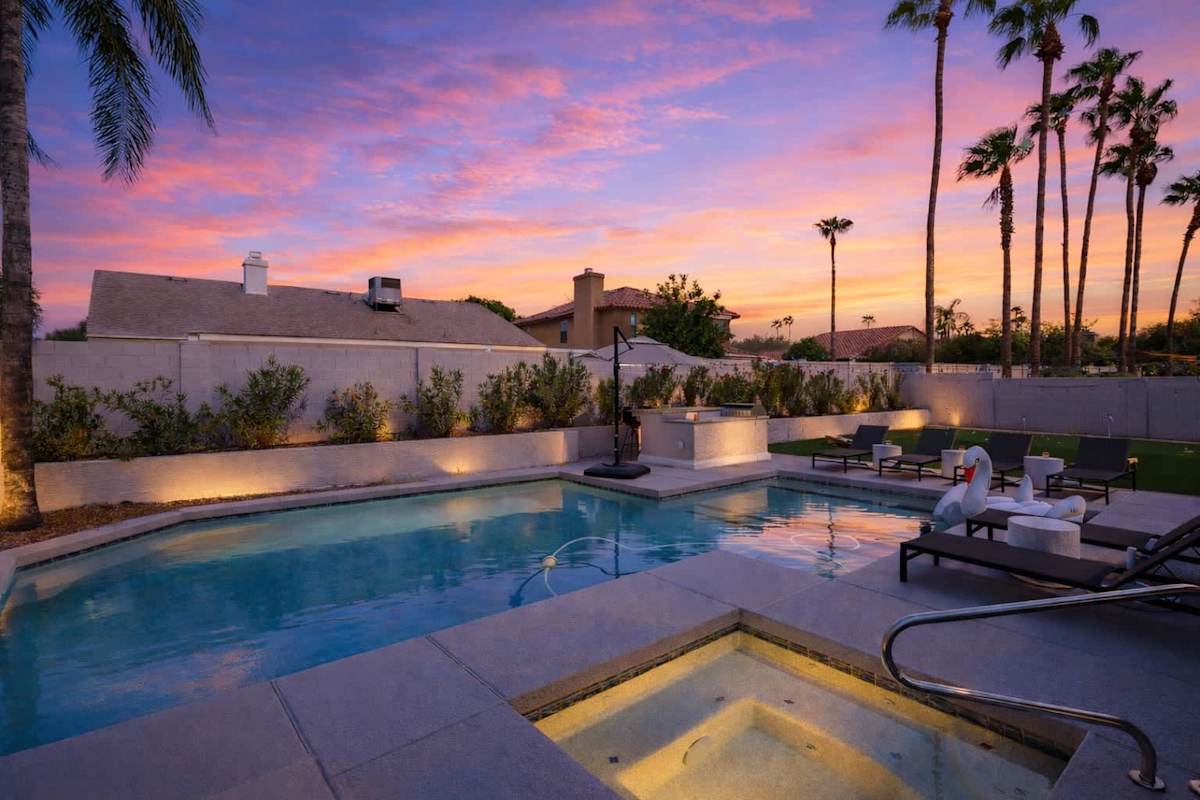 Backyard with putting green, corn hole, BBQ, bar seating, pool, jacuzzi, loungers, outdoor dining table and TV.