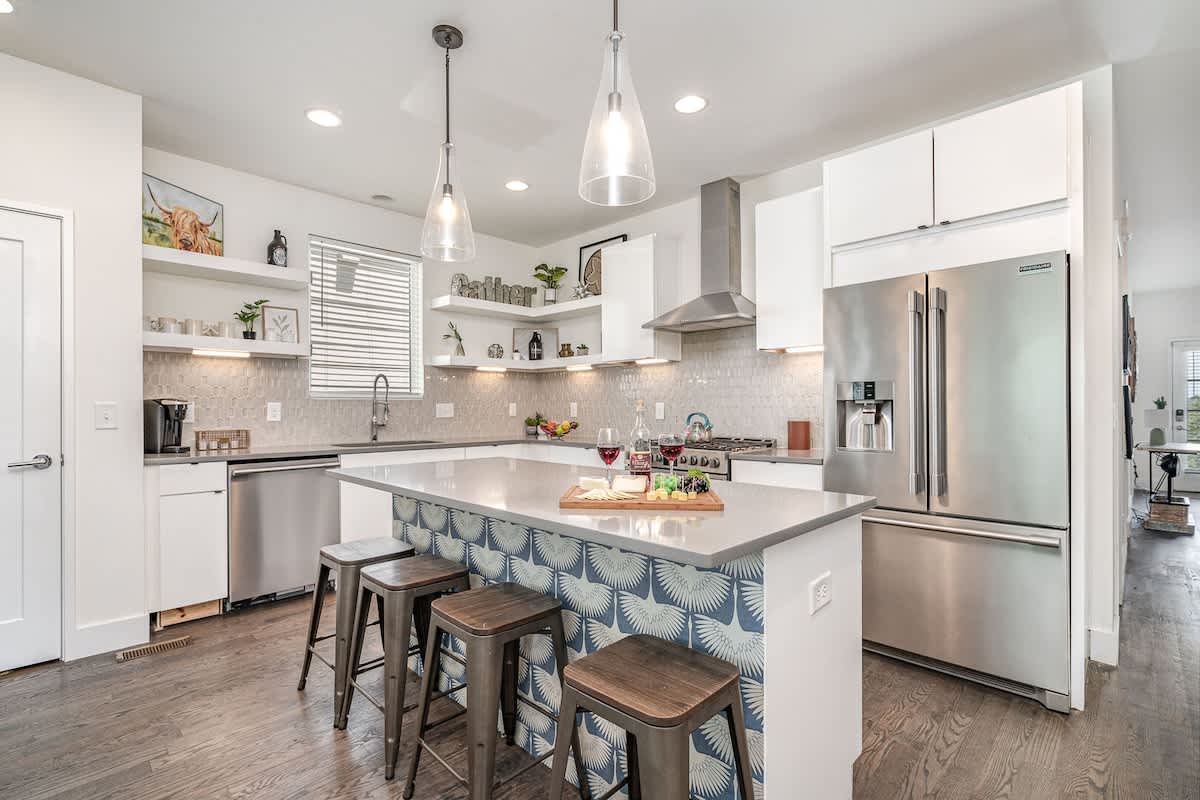 Unit 2: Bright open-concept kitchen featuring a quartz-topped island with bar seating, stainless steel appliances, and abundant natural light streaming through the windows.