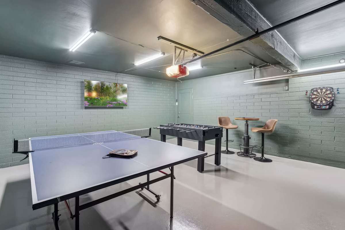 The game room delivers hours of fun with ping pong, foosball, a dartboard, bar-height seating, and a wall-mounted TV in a cool, brick-walled space.