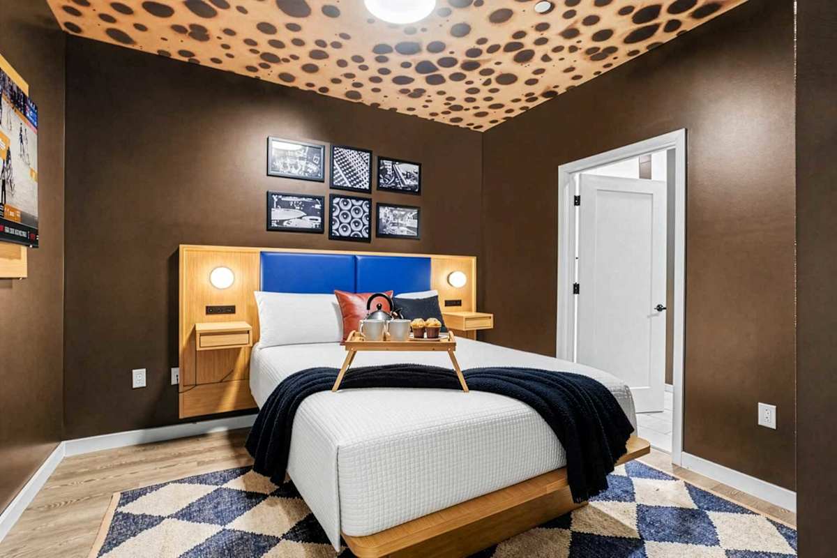 The primary bedroom wows with a cheetah print ceiling, rich brown walls, a queen bed with a bold blue headboard, gallery wall art, smart TV, closet space and a private en-suite bath.