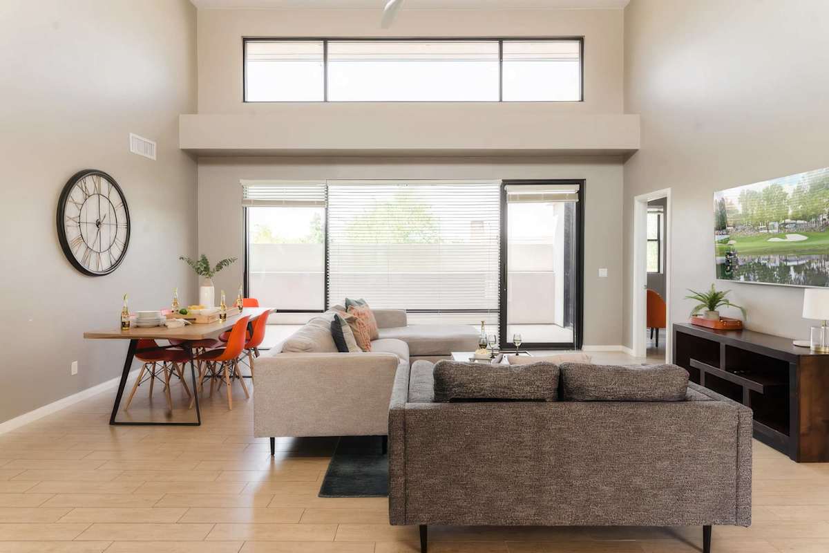 Unit 1: Spacious living room with soaring ceilings, a plush sectional, Smart TV, and an open concept flow to the kitchen and easy access to the private balcony.