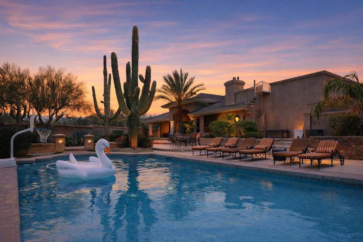 Resort-Style backyard featuring a large sparkling blue pool with a basketball hoop for friendly competitions in the water and sun loungers for basking in the valley of the sun!