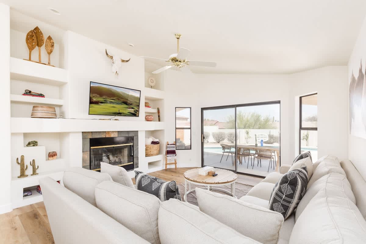 Bright open floor living space featuring a smart flat-screen TV, designer furnishings, and access to the outdoor patio with sparkling heated pool.