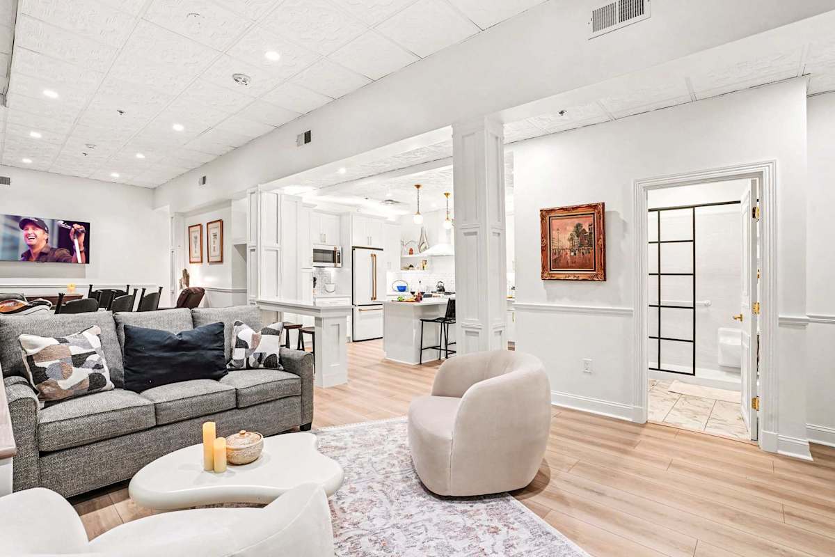 Relax in style in this bright living area, featuring a plush sofa, cozy swivel chairs, and a mounted TV, all open to the sleek white kitchen. Perfect for movie nights or casual conversation.