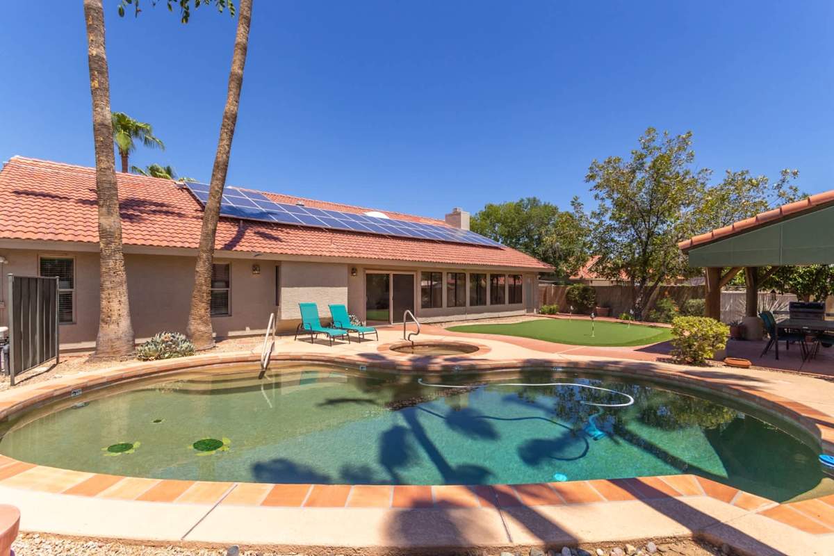 Spacious private yard with sparkling pool, spa, covered patio with outdoor dining table, BBQ grill, and putting green.