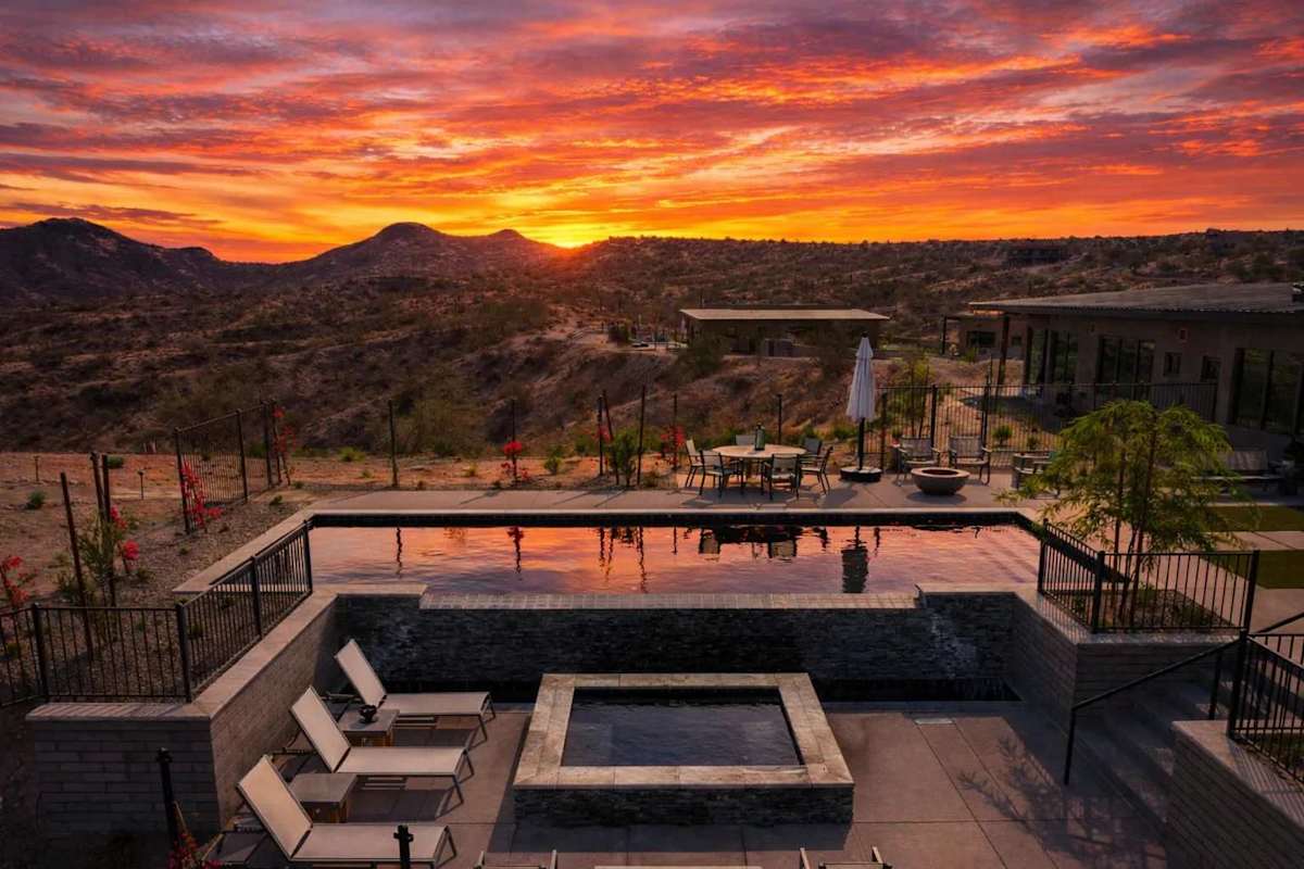 Stunning private oasis featuring a sparkling heated infinity pool and spa with sun loungers, a patio with a BBQ grill, multiple lounge areas, and fire pits surrounded by unparalleled desert views.