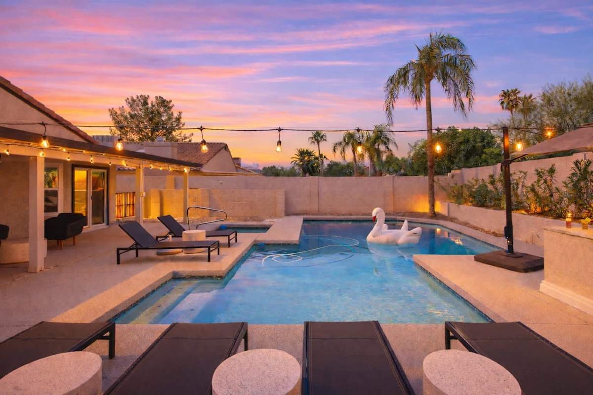 Backyard with putting green, corn hole, BBQ, bar seating, pool, jacuzzi, loungers, outdoor dining table and TV.