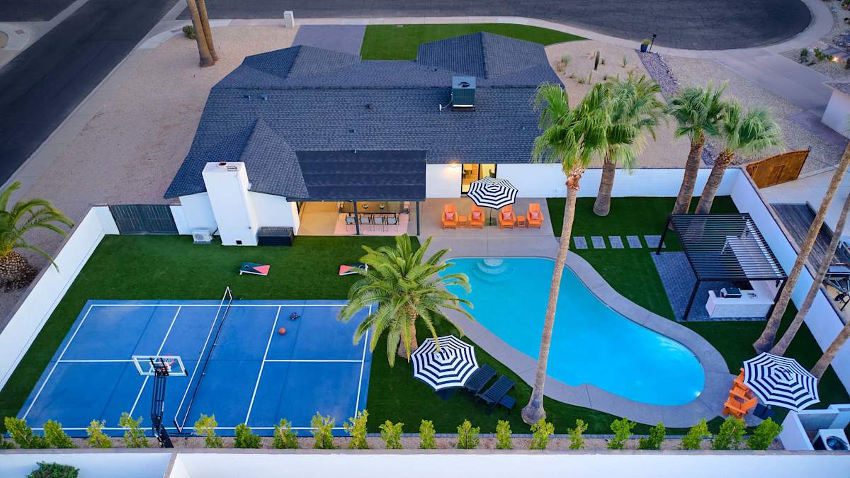 Resort-style backyard featuring a private pool, poolside loungers, a multi-sport court for basketball, pickleball, and tennis, turf with cornhole, a pergola with a built-in BBQ and bar seating, and a