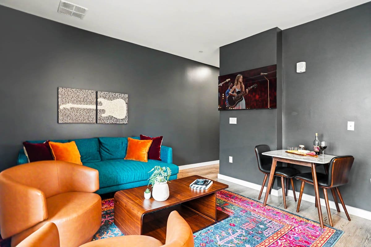 The living area brings bold personality with a teal sofa, leather swivel chairs, a sculptural wood coffee table, vibrant area rug, music-inspired art and a large smart TV.