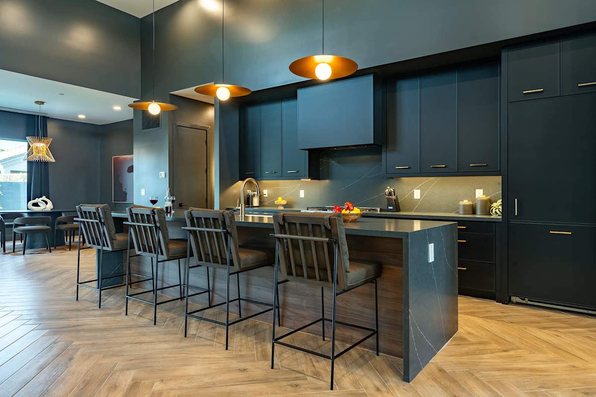 Gather in this sleek, modern kitchen featuring dark cabinetry, a spacious island with seating for four, and warm pendant lighting—perfect for casual meals or socializing.